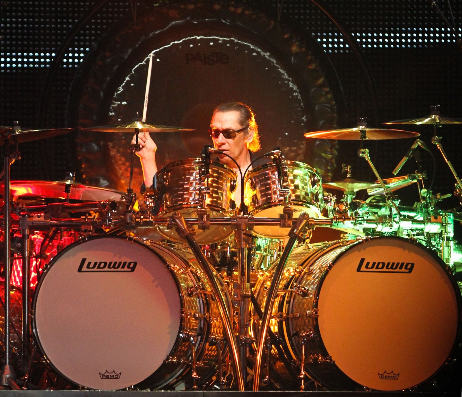 Alex Van Halen in sunglasses playing a chrome Ludwig drum kit in front of a large Paiste gong
