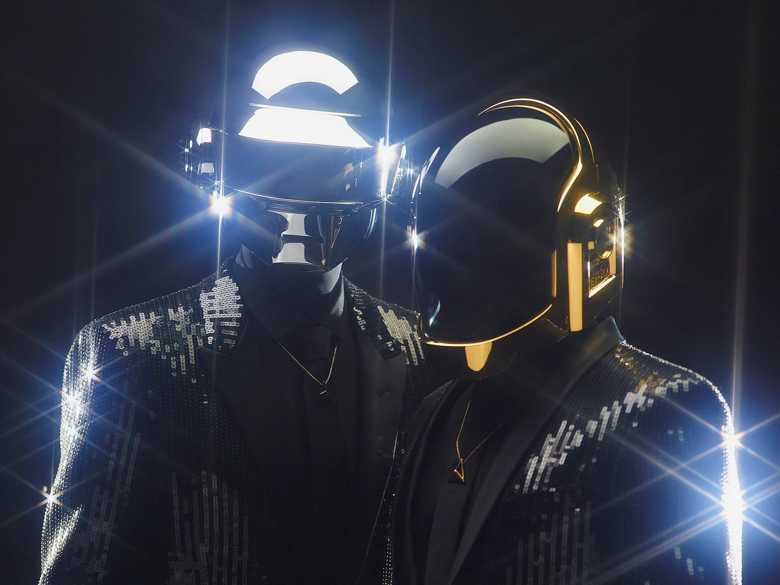 Daft Punk in silver and gold robot helmets and sequinned black jackets against a dark background