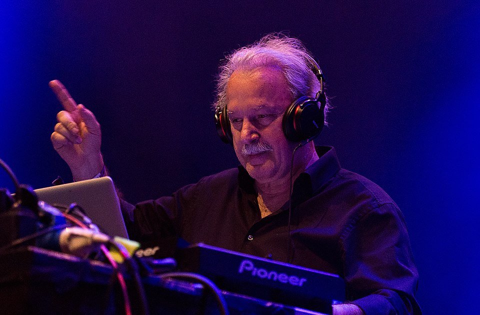 Giorgio Moroder wearing headphones and pointing while DJing on Pioneer equipment, lit in blue