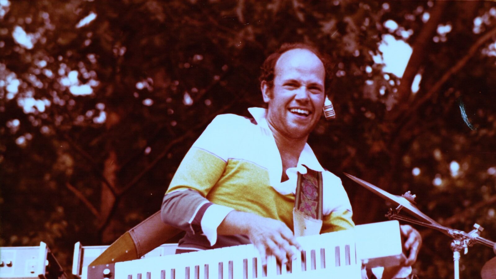 Jan Hammer smiling while playing a white keytar on an outdoor stage