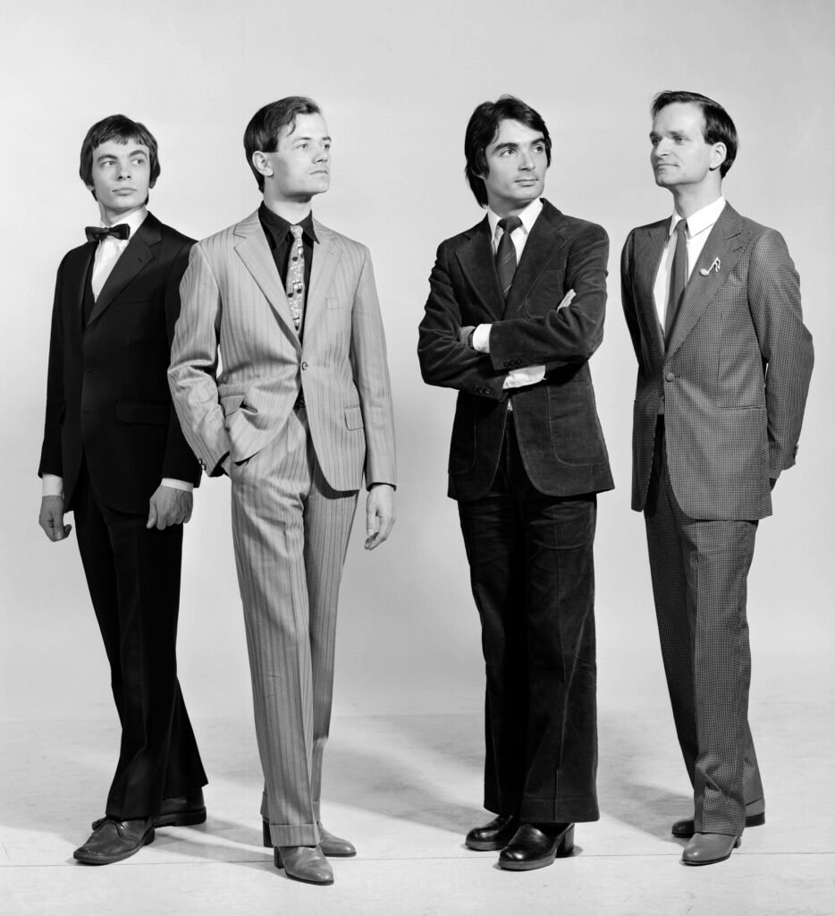 Black and white press photo of the four members of Kraftwerk in suits and short hair, 1975