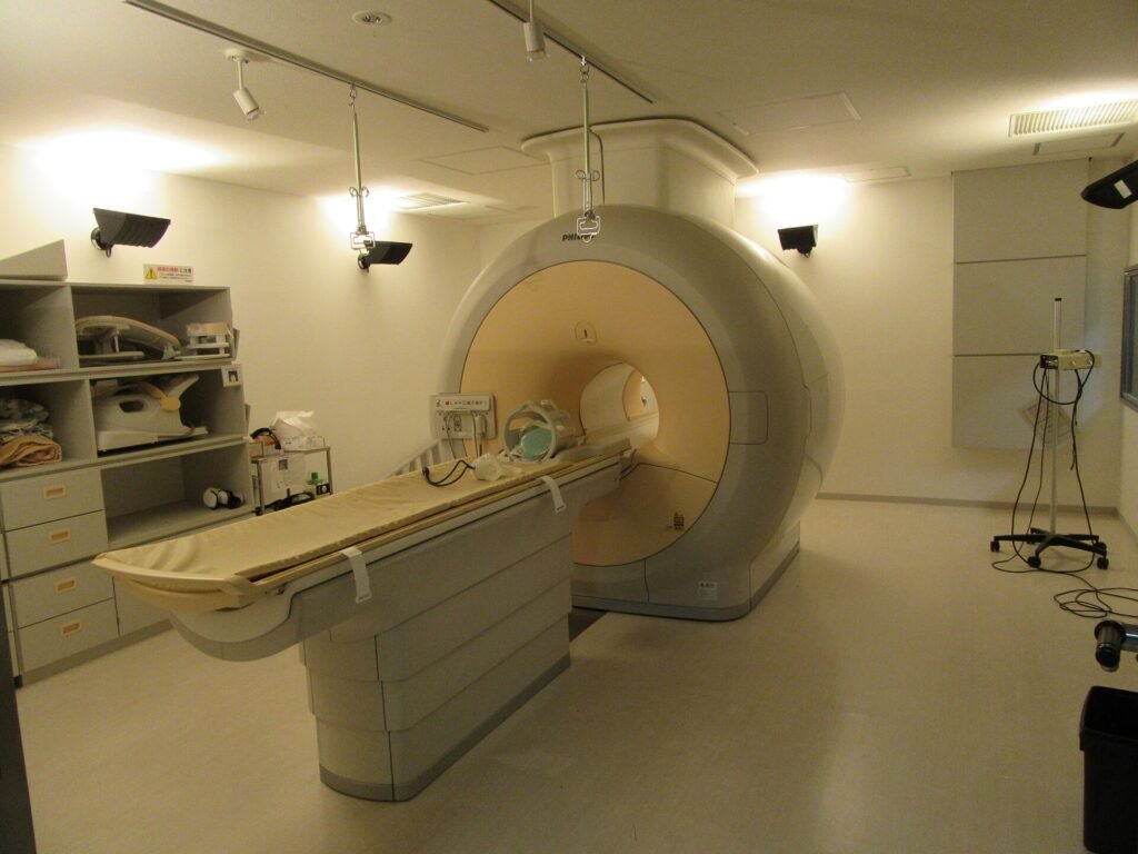 A white MRI scanner with a padded patient table in a softly lit hospital room