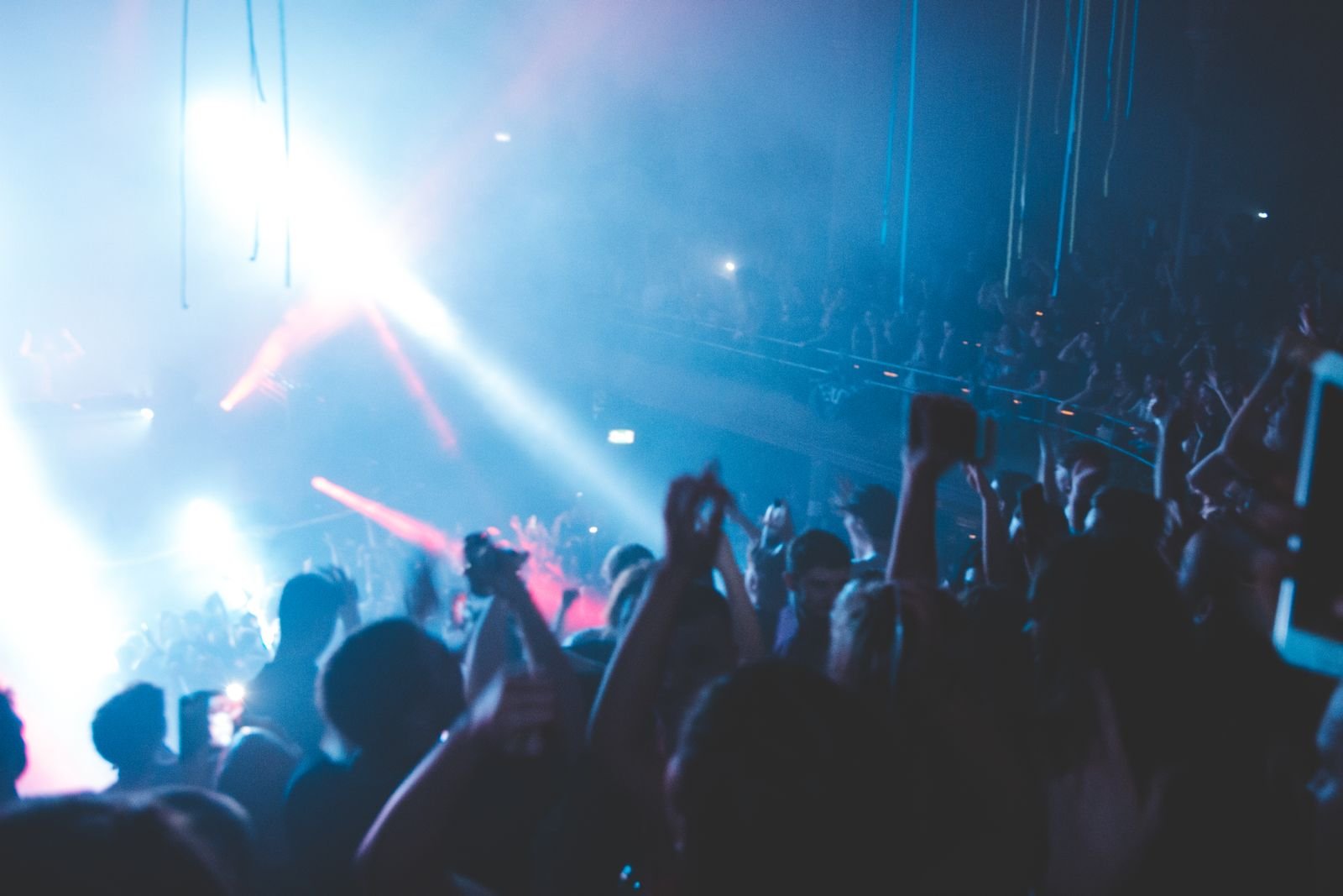 Crowd dancing with raised hands under stage lights at an electronic music concert