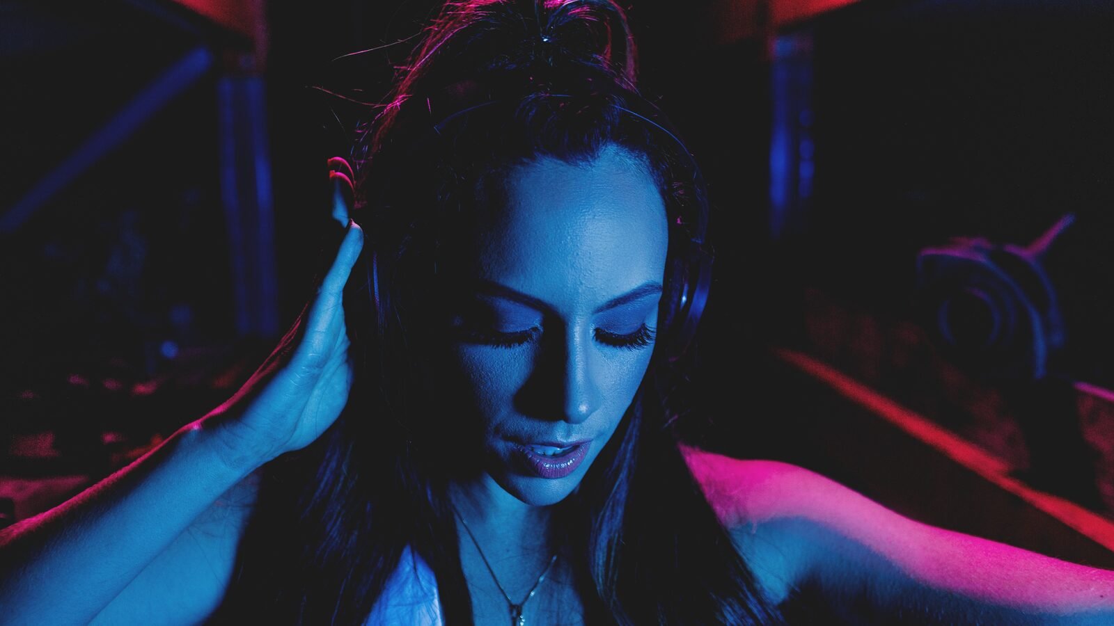 Young woman listening to music on headphones under blue and pink neon light