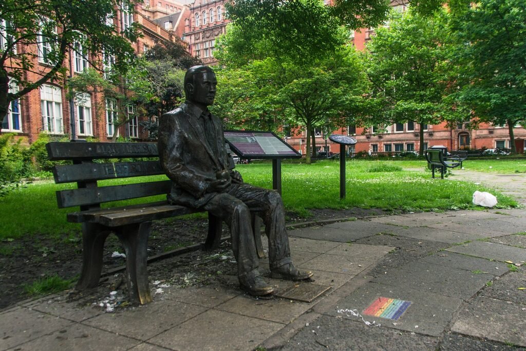 Bronze statue of Alan Turing sitting on a bench holding an apple in Sackville Gardens, Manchester
